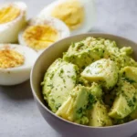Creamy avocado egg salad served in a bowl with herbs