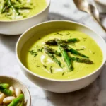 Bowl of creamy asparagus soup made without cream, garnished with fresh herbs.