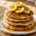 Stack of banana oat pancakes topped with syrup on a white plate