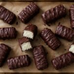 Chocolate-dipped coconut candy bars arranged on parchment paper with the coconut center visible in a few cut pieces