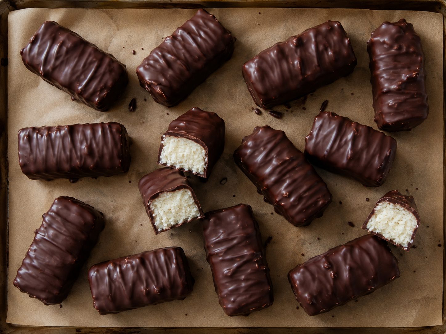 4-Ingredient Mounds Cookie Bars: Coconut Candy Bars Dipped in Melted Chocolate 4 Chocolate-dipped coconut candy bars arranged on parchment paper with the coconut center visible in a few cut pieces