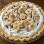 Whole Banana Cream Pie topped with whipped topping, banana slices, and chocolate shavings in a glass pie plate