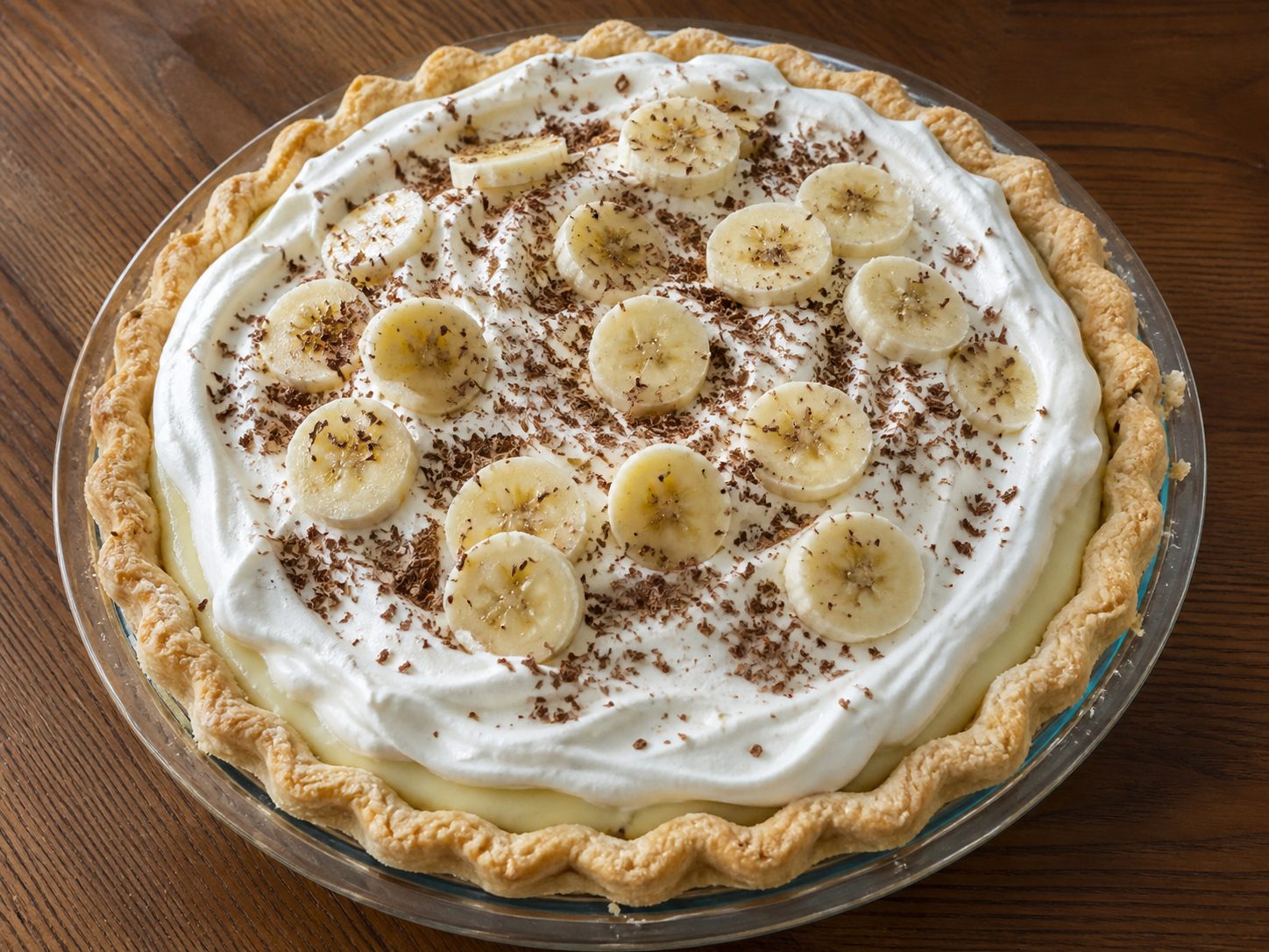 Whole Banana Cream Pie topped with whipped topping, banana slices, and chocolate shavings in a glass pie plate
